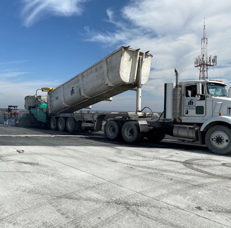 Tráiler con caja térmica descargando mezcla asfáltica en una pavimentadora